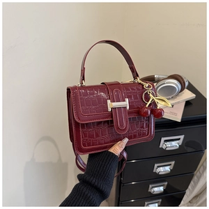Detail of dark red croc-embossed patent leather handbag with gold H-buckle and cherry charm