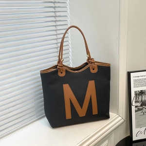 Large black woven tote bag with brown leather handles and prominent letter M logo