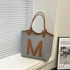 Grey woven tote bag with large brown leather M letter and slim shoulder straps
