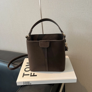 Deep brown suede bucket bag with top handle and adjustable shoulder strap on a prop book