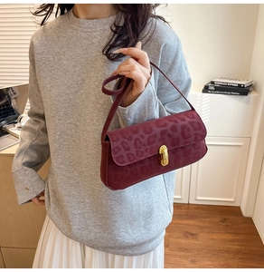 Detail of burgundy leopard print underarm bag with gold oval twist lock on suede texture