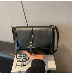 Detail shot of the black faux leather texture and gold rectangular buckle on the bag