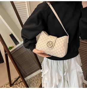 Close-up of a beige shoulder bag with letter monogram pattern and gold M-logo buckle