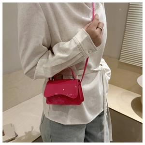 Close-up of a glossy rose red patent leather mini square bag with top handle and strap