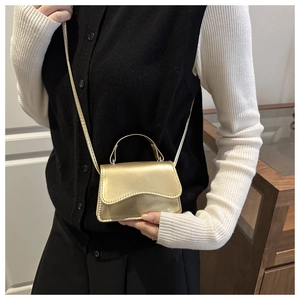 Mini metallic gold crossbody bag styled with a white knit top and black vest
