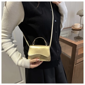 Detail of a mini gold metallic handbag with streamlined flap and slim strap in a cozy setting