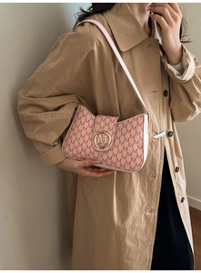 Close-up of pink monogram shoulder bag with gold M-logo buckle worn with a beige trench coat