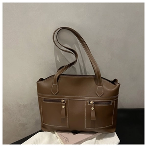 Detail of dark brown leather tote featuring symmetrical front zipper pockets and white stitching