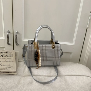 Sac à main matelassé argenté avec motif à carreaux et breloque sur un canapé