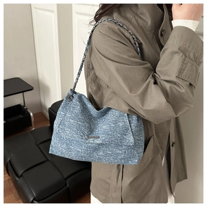 Close-up of blue textured tote bag with metal chain strap worn by a model