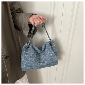 Detailed texture of blue denim tote bag featuring vintage wash and dark grey metal chain