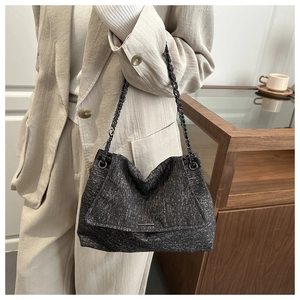 Detail of dark grey textured tote bag with metal chain strap and flap closure