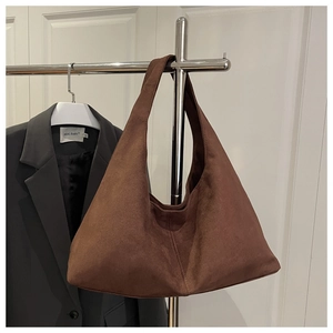 Detail of a brown suede hobo bag hanging on a stainless steel rack with a grey blazer