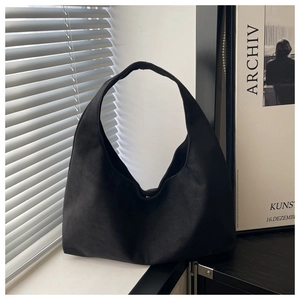 Detail view of the black faux suede shoulder bag with minimalist curved silhouette