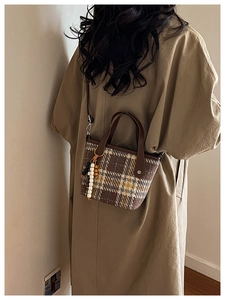 Detail of a brown plaid bucket bag featuring wooden bead charms and a shoulder strap