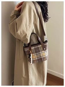 Detail view of retro plaid tote bag with brown leather trim and beaded charm accessory