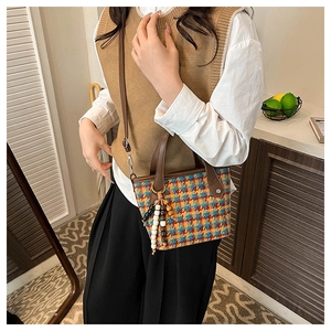 Close-up of multicolor houndstooth tote bag with brown leather straps and beaded charm