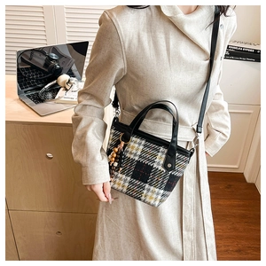 Detail of checkered tote bag featuring black handles and wooden bead charm accessory