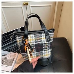 Detail of retro houndstooth tote bag featuring wooden bead tassel and black leather handles