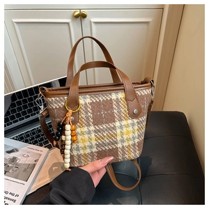 Detailed close-up of plaid tote bag with beaded tassel and brown faux leather handle