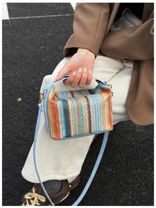 Rainbow striped straw tote bag featuring light blue leather straps held by a model