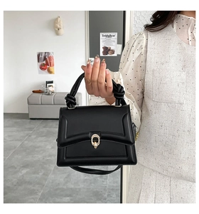 Detail of black trapezoid leather bag with gold ring buckle and knotted handle decoration