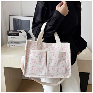 Detail of white corduroy tote bag showing pink bow prints and dual front pockets