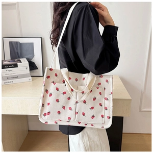Detail of cream corduroy tote bag featuring red strawberry prints and outer pockets