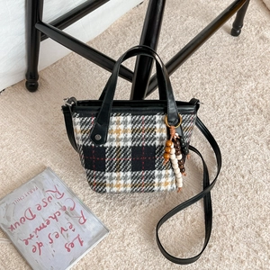 Retro plaid wool tote bag with beaded charm and leather handles on a plush rug