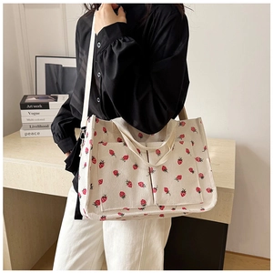 Close-up of beige corduroy tote bag with red strawberry pattern and side pockets