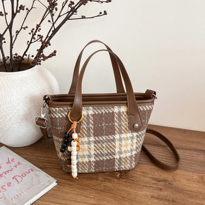 Retro brown plaid tote bag with leather handles and colorful beaded charm in warm setting