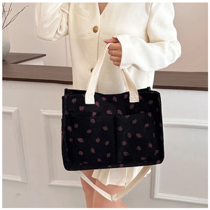 Detail of black corduroy tote bag with pink strawberry embroidery and front pockets