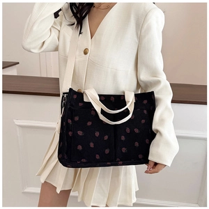 Detail of black corduroy tote bag with strawberry patterns and cream shoulder straps