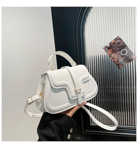 Detail of white wave-flap handbag showing metallic gold clasp and textured faux leather