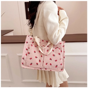 Detailed macro view of pink corduroy tote bag featuring red strawberry print and front pockets
