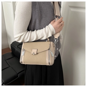 Detail of beige canvas shoulder bag with silver zippers and lettered strap design