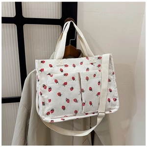 Detail of white corduroy tote bag featuring red strawberry print and front utility pockets