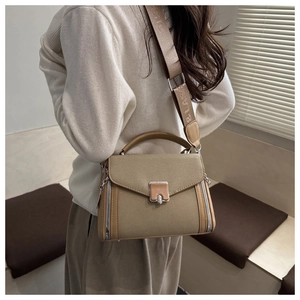 Close-up of khaki crossbody bag with wide embroidered strap and metallic zipper detail