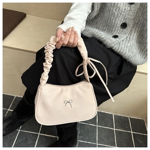 Detalle de bolso media luna blanco crema con lazo plateado y asa de textura plisada