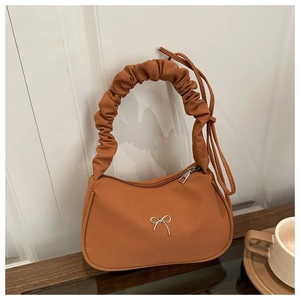 Détail d'un sac croissant orange-brun avec anse plissée et nœud métallique argenté