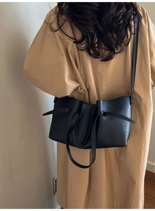 Detail view of a black knotted tote bag styled with a khaki trench coat for a chic look