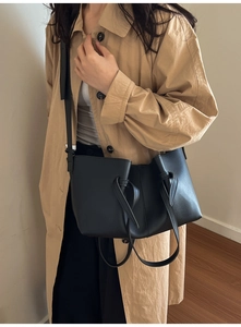 Détail d'un grand sac cabas plissé noir avec nœuds latéraux porté sur un trench-coat