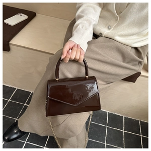 Detail of dark brown patent leather handbag with gold chain strap in hand