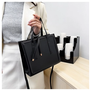 Détail d'un sac bandoulière minimaliste noir en cuir avec doubles poignées et une sangle