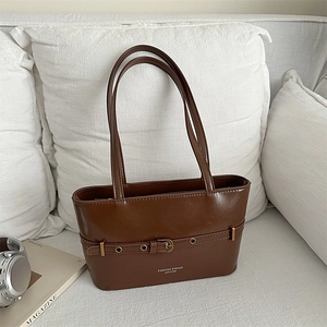 Sac fourre-tout en cuir marron foncé avec ceintures décoratives sur un canapé blanc chic