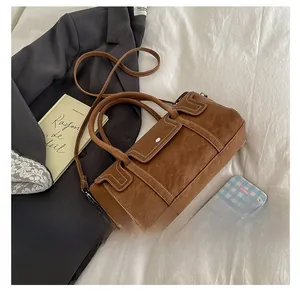 Close-up of brown suede Boston bag with white stitching on white bedding background