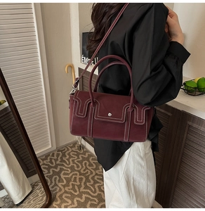Close-up of burgundy frosted leather handbag with white stitching and metal buckle