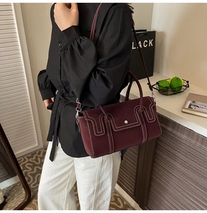 Close-up of burgundy leather handbag with white contrast stitching and gold metal buckle