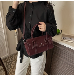 Détail du sac bandoulière bordeaux avec surpiqûres blanches et boucle argentée élégante