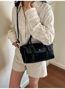 Detail of a black crossbody bag featuring contrast white stitching and structured handles